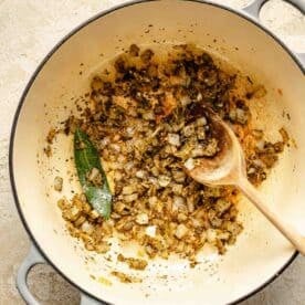 onions, garlic, seasonings, and bay leaf in a dutch oven with a wooden spoon