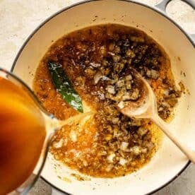 adding broth to the dutch oven with the onions, bay leaf, and seasonings