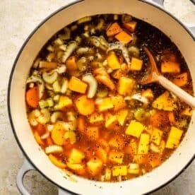 a wooden spoon is in the soup along with celery and carrots visible