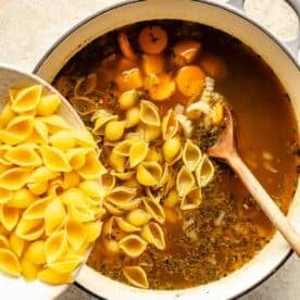 dry pasta shells are being poured into the soup mixture
