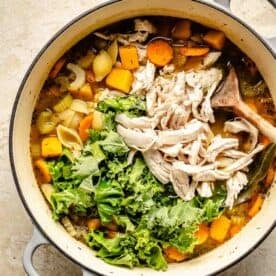 shredded turkey and kale leaves are added to the top of the soup in the dutch oven