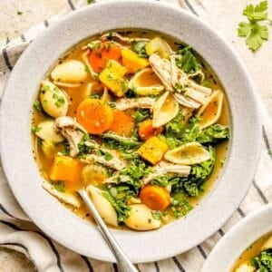 a bowl of turkey vegetable soup sits on top of a striped linen towel with a metal spoon in the bowl