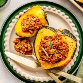 A plate with stuffed acorn squash, filled with rice and herbs. A knife and fork are placed beside the squash.