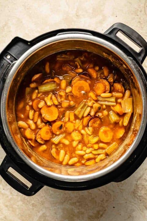 Instant pot containing a cooked white bean and sausage soup with sliced carrots, beans, celery, and a rich broth.