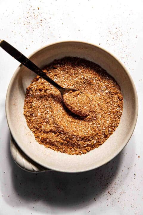 A bowl filled with bbq dry rub seasoning mix and a spoon, placed on a white surface.