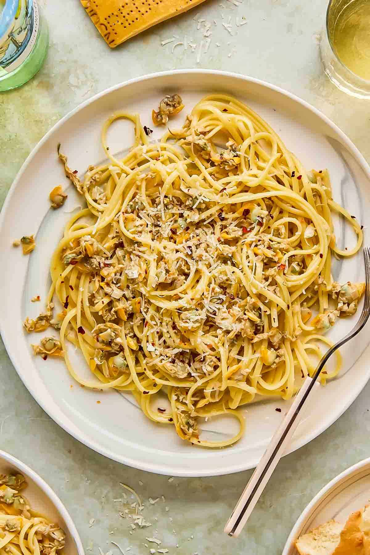 A plate of linguine with clams, garnished with grated cheese and red pepper flakes, accompanied by a fork.