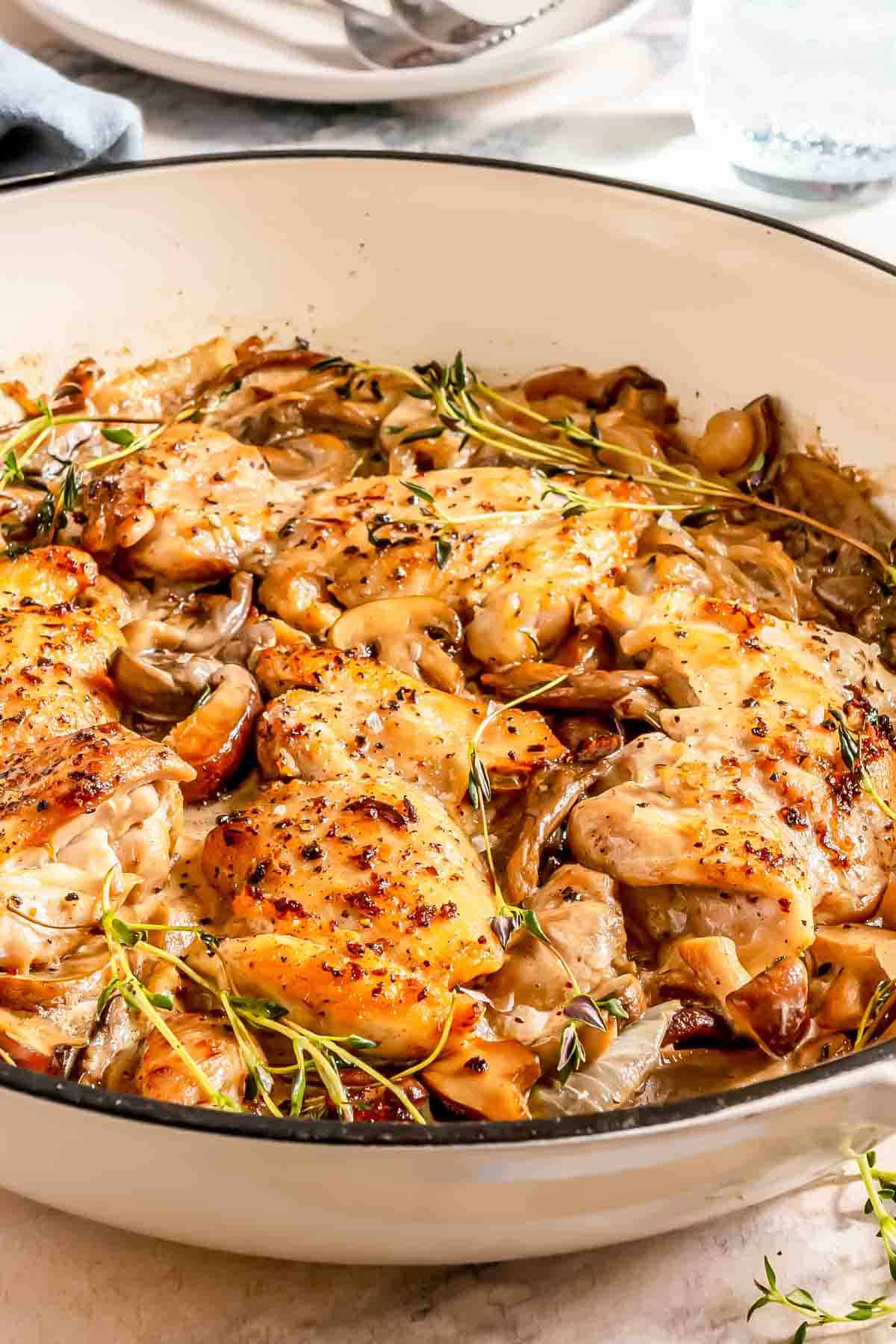 Chicken thighs cooked with mushrooms and onions in a skillet, garnished with fresh thyme.