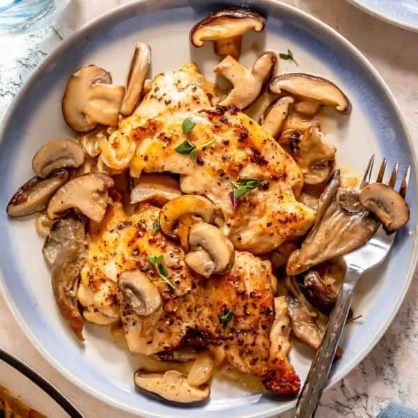 Creamy mushroom chicken served with a creamy mushroom sauce and garnished with fresh herbs on a round plate, accompanied by a fork and knife.