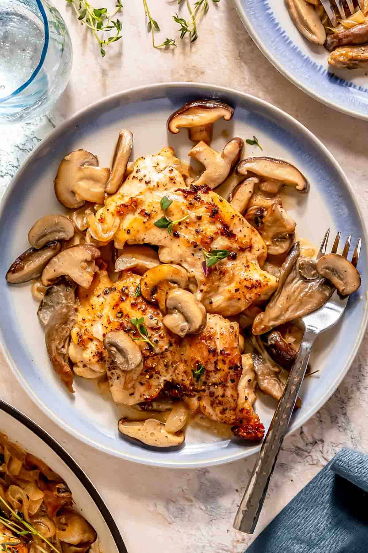 Creamy mushroom chicken served with a creamy mushroom sauce and garnished with fresh herbs on a round plate, accompanied by a fork and knife.