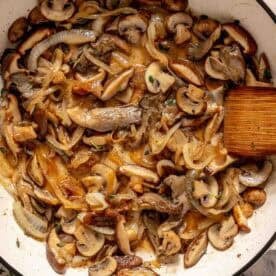 Sautéed mushrooms and onions in a white skillet with a wooden spatula.