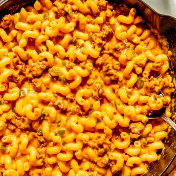 A skillet filled with creamy chorizo mac and cheese mixed with ground meat and sauce, with a spoon on the side.