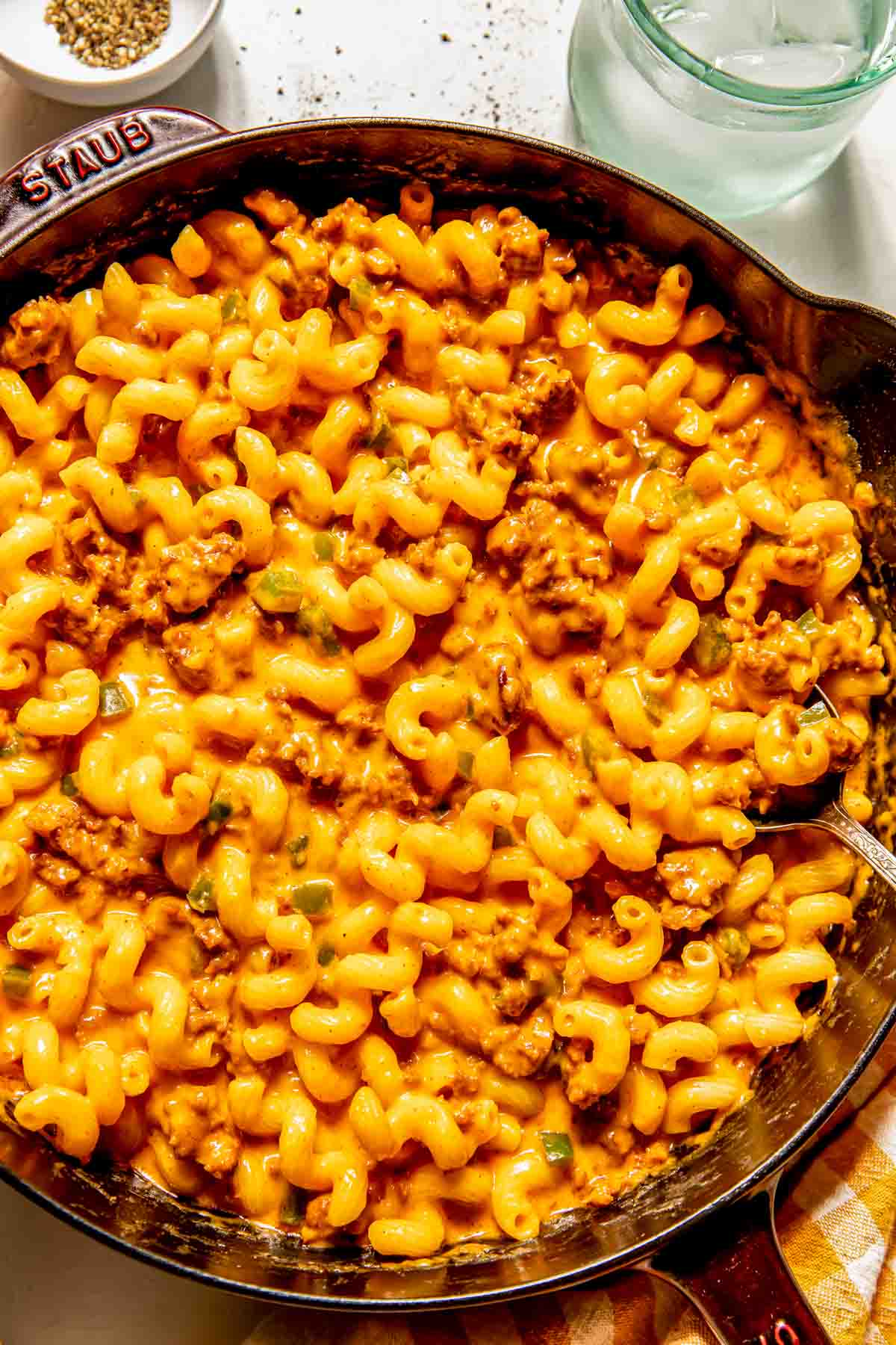 A skillet filled with creamy chorizo mac and cheese mixed with ground meat and sauce, with a spoon on the side.