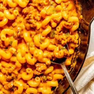 A skillet filled with cheesy macaroni pasta mixed with ground chorizo and a metal spoon resting inside.