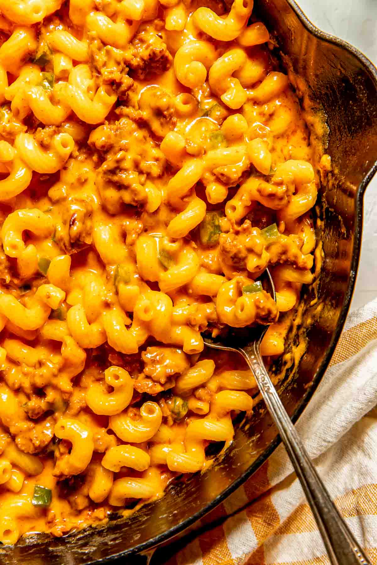 A skillet filled with cheesy macaroni pasta mixed with ground chorizo and a metal spoon resting inside.
