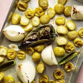 Roasted tomatillos, onion quarters, jalapeños, and a poblano pepper arranged on a metal baking sheet.