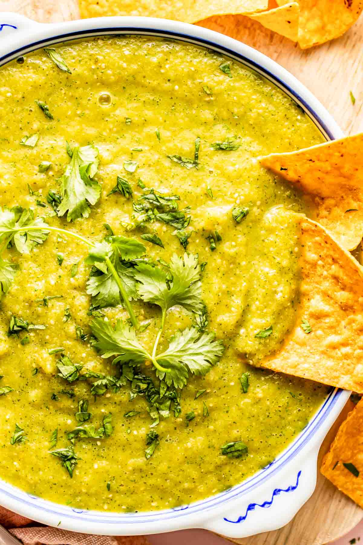 A bowl of green salsa garnished with fresh cilantro, surrounded by tortilla chips.