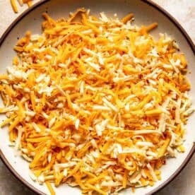 A bowl filled with a mixture of shredded yellow and white cheese on a light-colored surface.