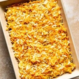 A rectangular baking dish filled with uncooked casserole topped with a layer of shredded cheese.