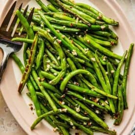 A plate of roasted garlic green beans with a serving fork on the side.