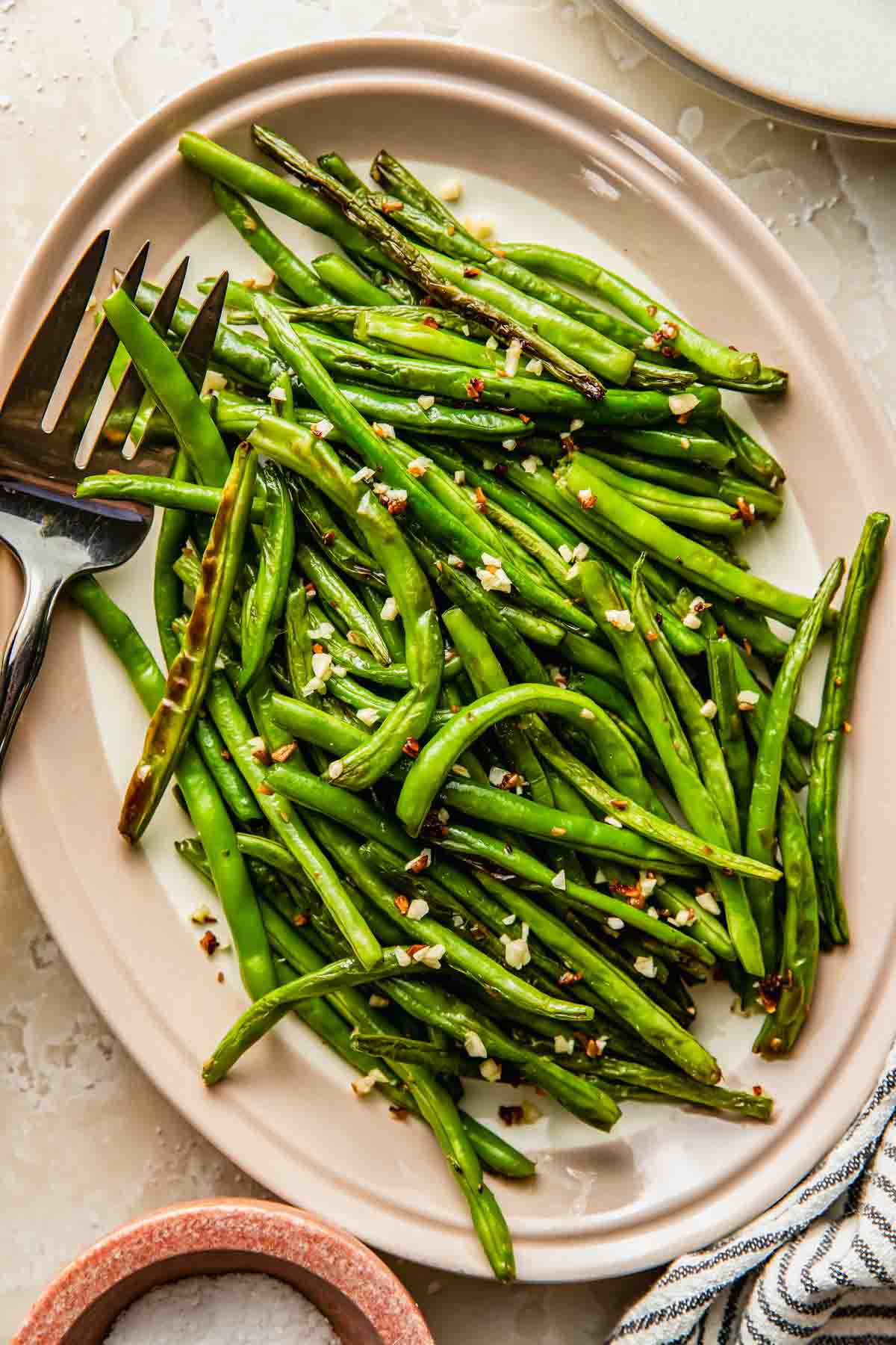 A plate of roasted garlic green beans with a serving fork on the side.