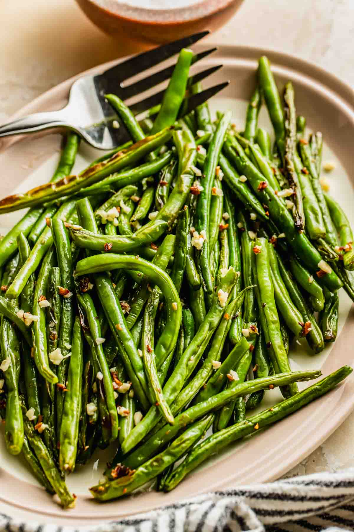 A plate of roasted garlic green beans with a fork resting on the plate.