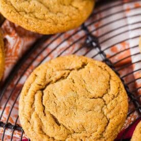 Close-up of round, golden-brown ginger molasses cookies cooling on a black wire rack over a colorful cloth.
