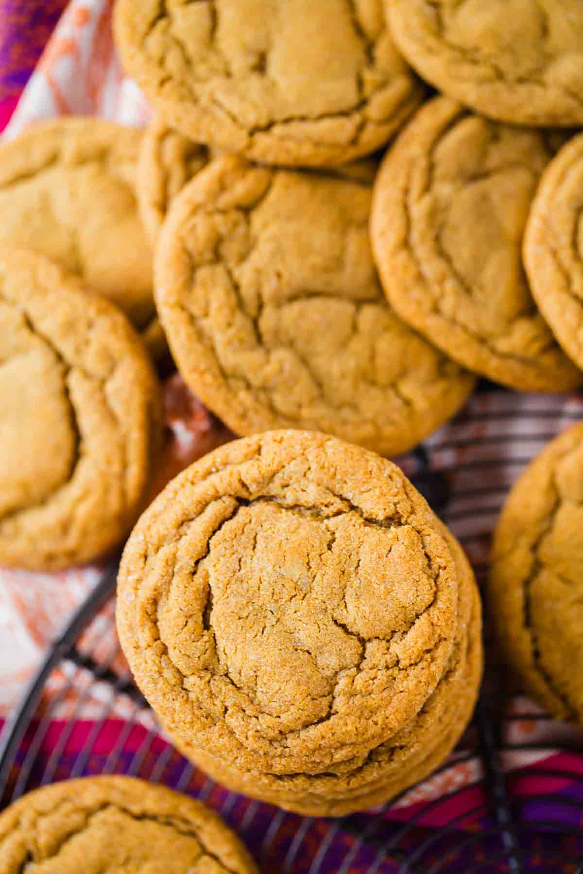 A close-up of several golden brown, soft-baked ginger molasses cookies with cracked surfaces arranged in a pile on a wire rack.