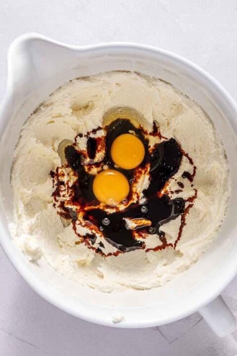 A mixing bowl with creamed butter and sugar, two raw eggs, and molasses on top, ready to be mixed.