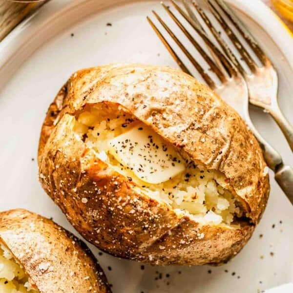 A baked potato split open on a plate, topped with butter and black pepper, with a fork and knife beside it.