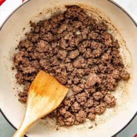 Cooked ground beef in a red pot with a wooden spatula, shown from above.