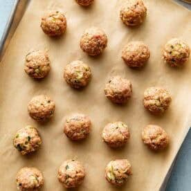 Uncooked meatballs arranged in rows on a parchment-lined baking sheet.
