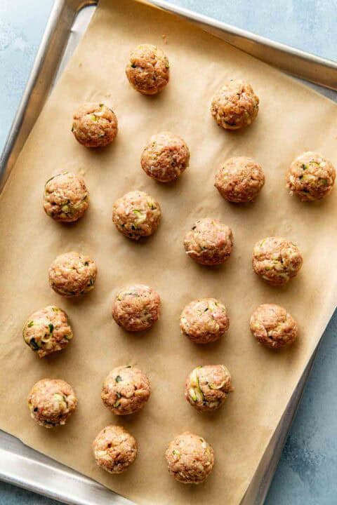 Uncooked meatballs arranged in rows on a parchment-lined baking sheet.