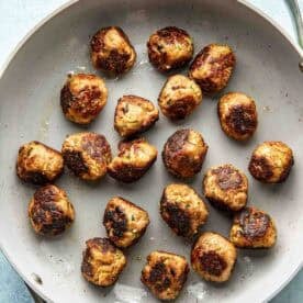 A skillet containing evenly spaced, browned meatballs on a light surface.