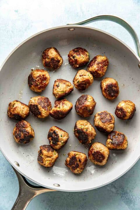 A skillet containing evenly spaced, browned meatballs on a light surface.