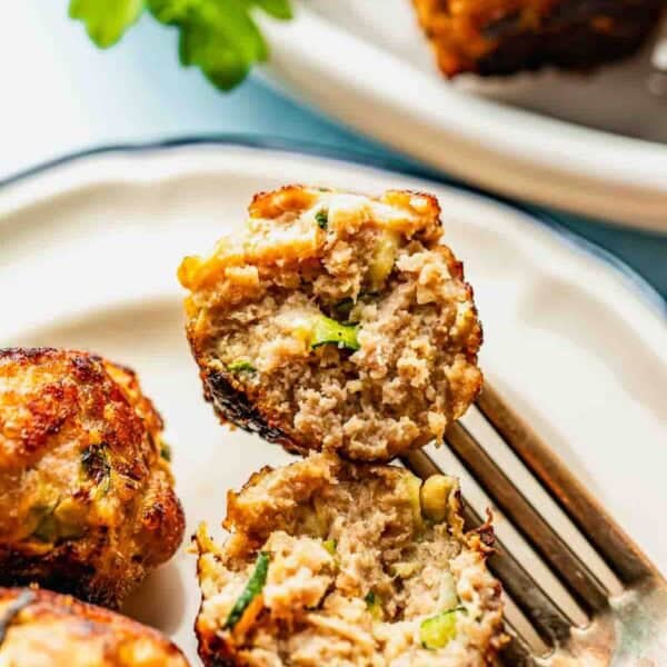 A close-up of a plate with meatballs, one cut open with a fork to show the inside texture and ingredients like herbs and vegetables. Parsley garnish is visible in the background.