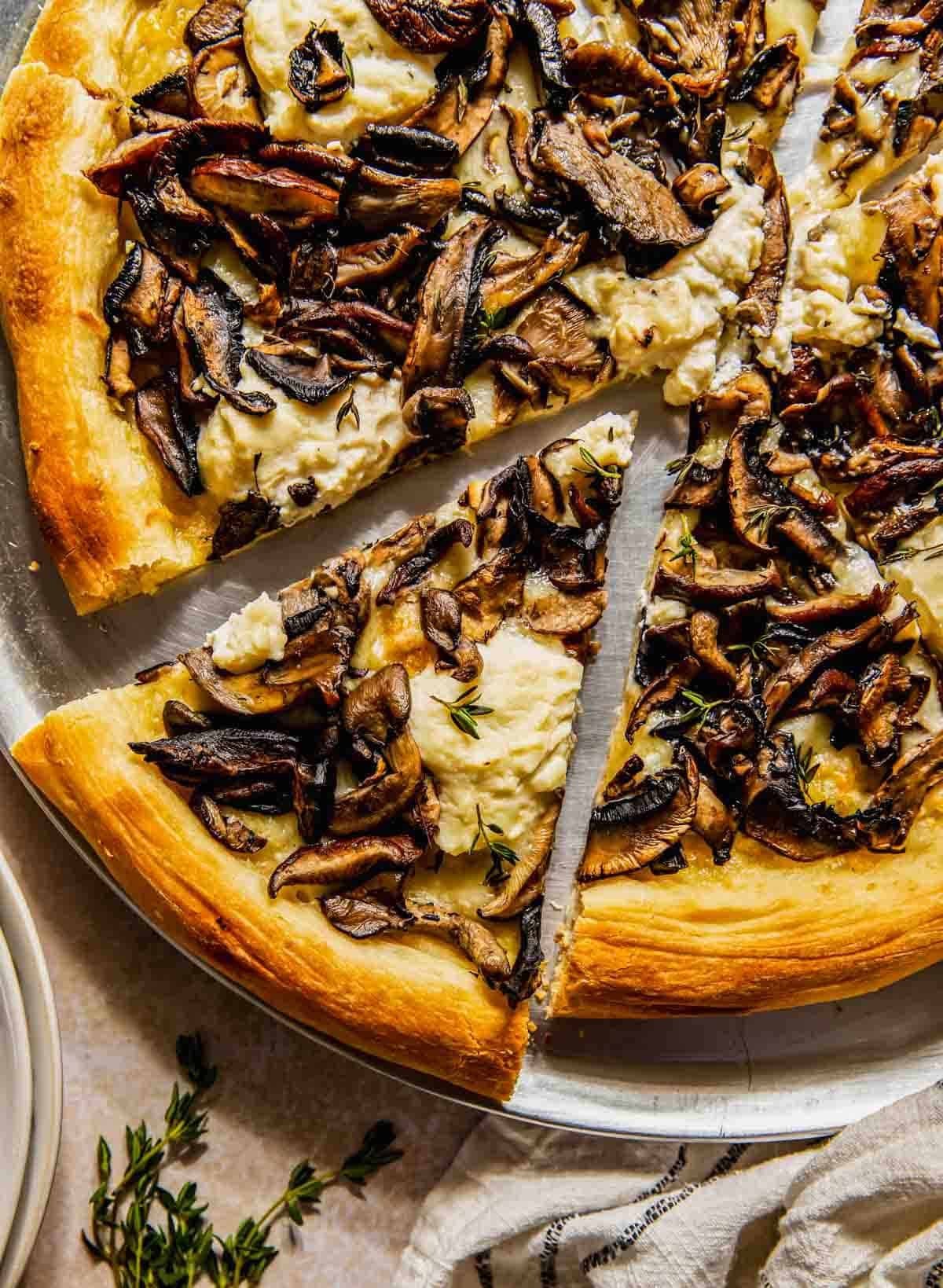 Nahaufnahme von Pizzastücken mit Ricotta-Käse und gebratenen Pilzen auf einem runden Metalltablett.