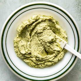 A white bowl filled with thick pesto with a white spatula resting inside.