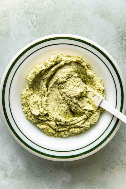 A white bowl filled with thick pesto with a white spatula resting inside.