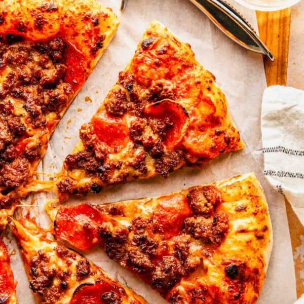 Overhead view of sliced pepperoni and sausage pizza on parchment paper, with a pizza cutter and a glass nearby.