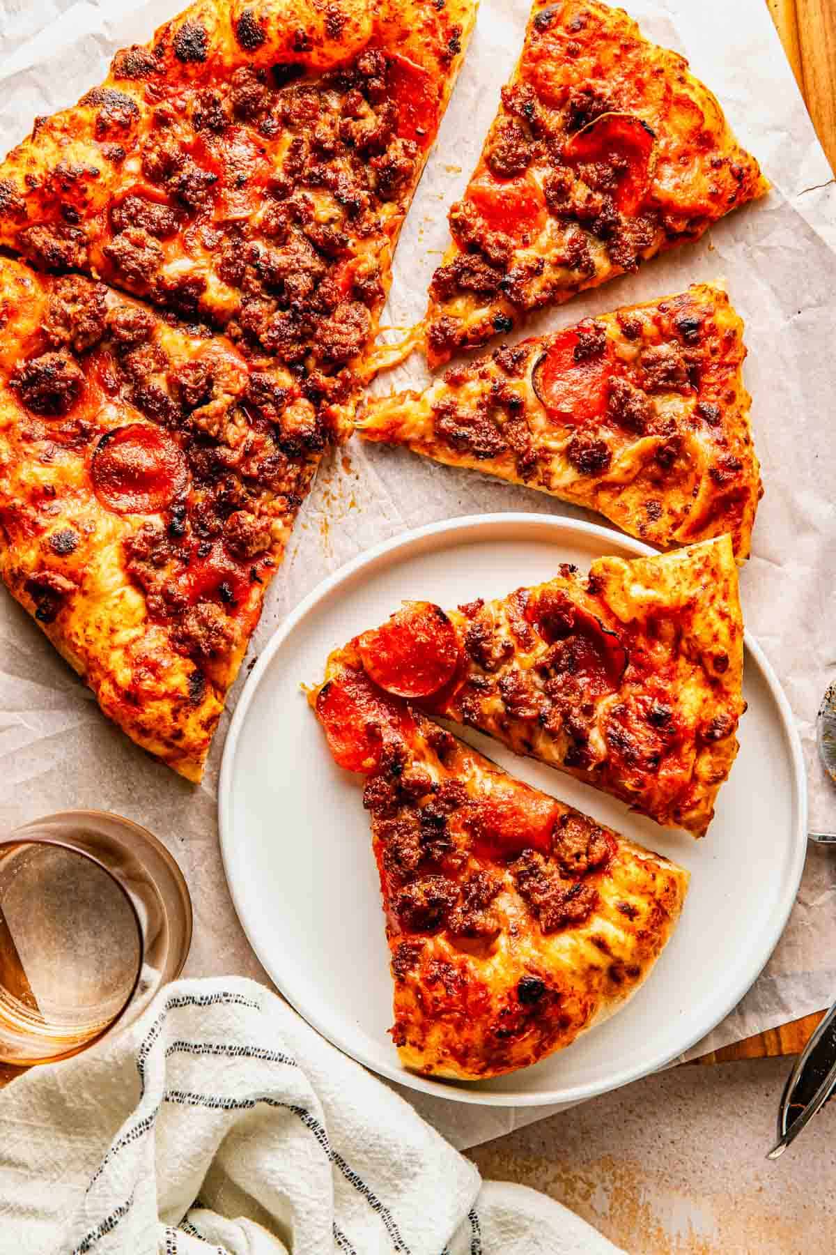 A pepperoni and sausage pizza cut into slices, with two slices served on a white plate and a glass of water nearby.