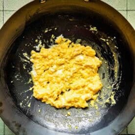 Scrambled eggs cooking in a black wok on a tiled surface.