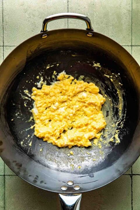 Scrambled eggs cooking in a black wok on a tiled surface.