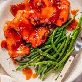 Plate with boneless chicken thighs topped with red sauce, served alongside a portion of cooked green beans and a fork on the side.