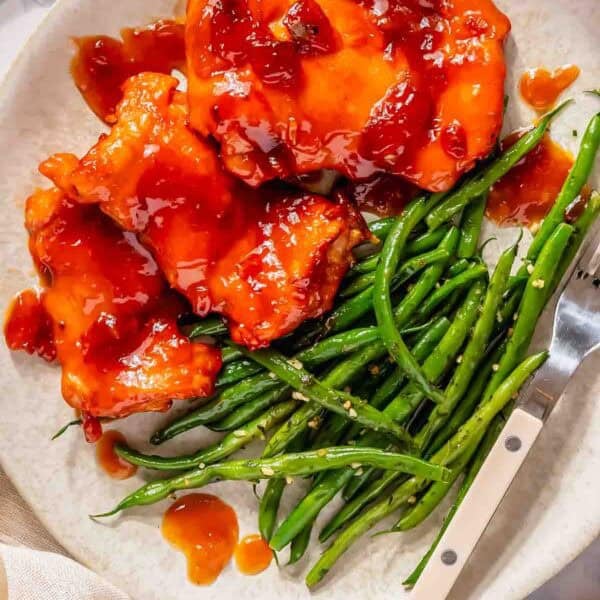 Plate with boneless chicken thighs topped with red sauce, served alongside a portion of cooked green beans and a fork on the side.