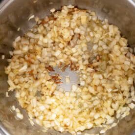 Chopped onions sautéing in the bottom of a stainless steel pot, starting to turn translucent with some browning visible.