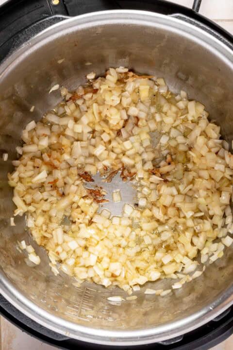 Chopped onions sautéing in the bottom of a stainless steel pot, starting to turn translucent with some browning visible.