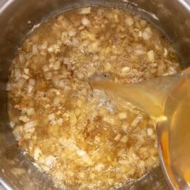 Chopped onions and garlic are sautéed in an Instant Pot, while broth is being poured in, viewed from above.