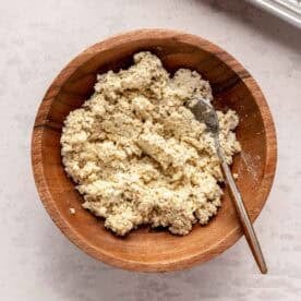 A wooden bowl filled with breadcrumb topping and a fork, placed on a light-colored countertop.