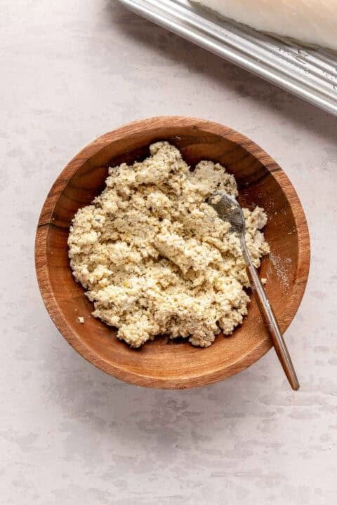 A wooden bowl filled with breadcrumb topping and a fork, placed on a light-colored countertop.