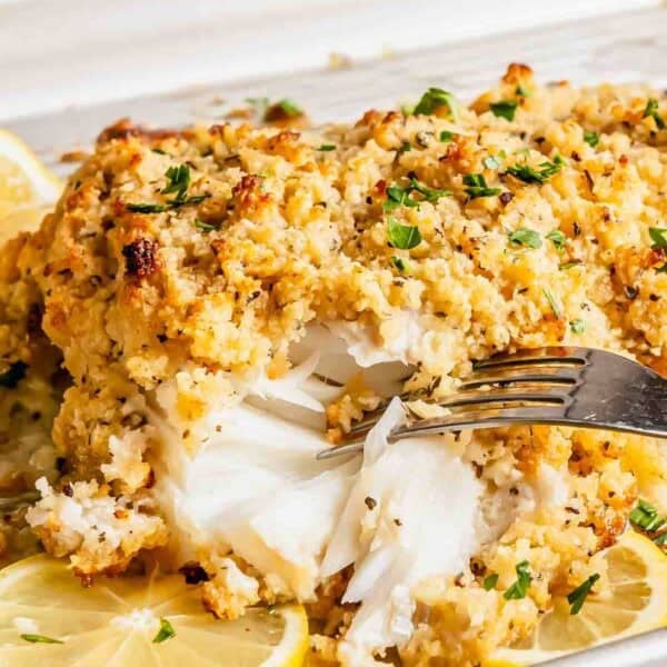 Baked crispy haddock with a golden breadcrumb crust, garnished with parsley and lemon slices, being flaked with a fork.